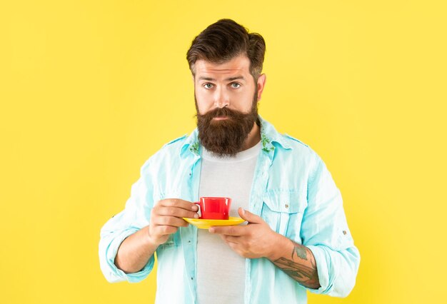 Serious caucasian man hold cup and saucer yellow background tea