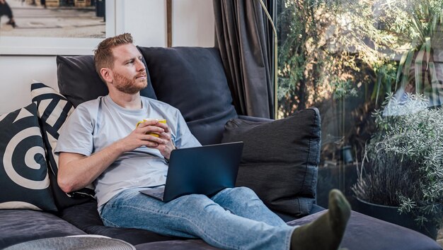 Serious caucasian man looking through the window holding a cup