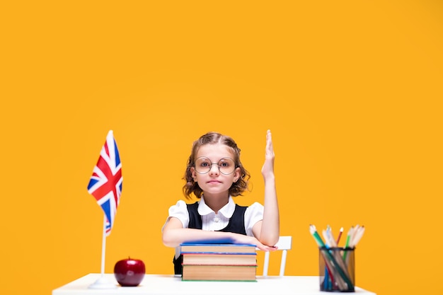 Серьезная кавказская школьница сидит за столом и поднимает руку на уроке английского флага великобритании