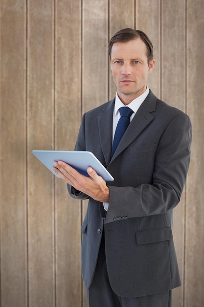 Serious charismatic businessman holding a tablet computer against wooden surface with planks