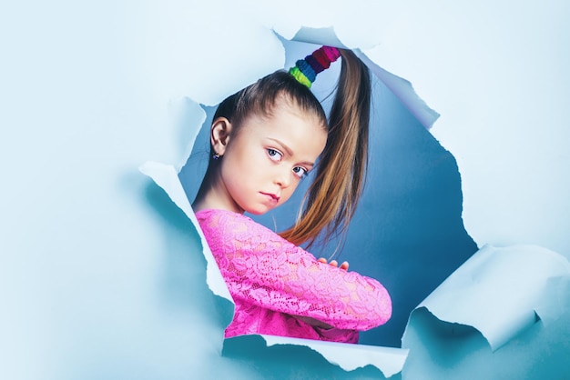 Serious child girl looking out of a paper hole banner happy girl