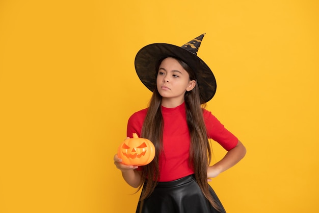 Serious child in witch hat hold pumpkin on yellow background trick or treat