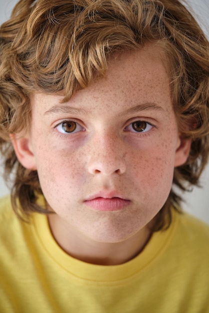 Serious child in yellow casual wear with brown hair and freckles looking at camera