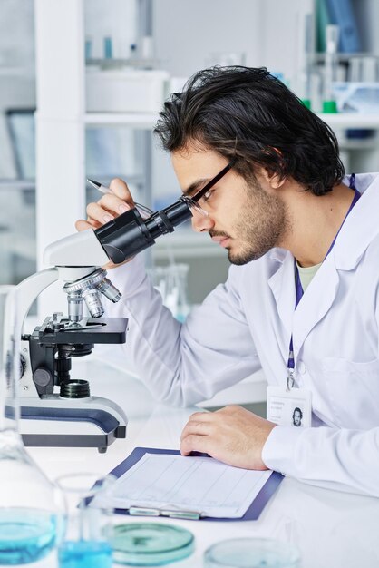 Serious clinician studying bacteria or new virus in microscope in laboratory