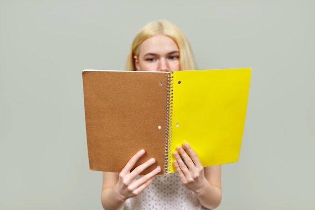 Serious college student reading notebook, close up yellow cover place for text. Girl teenager on light studio background