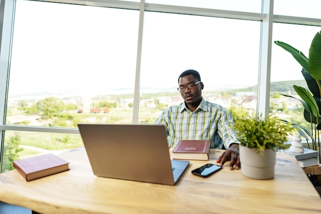 Serious concentrated african man studying or working with laptop indoors