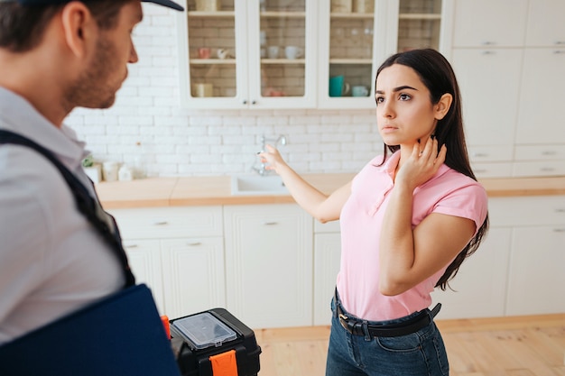 Serious concentrated woman stand with plumber in kitchen