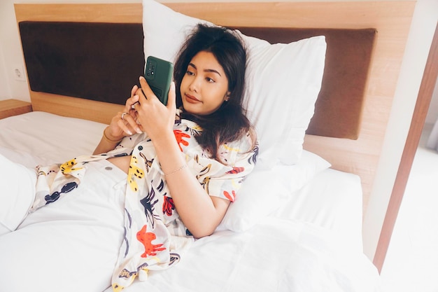 Serious concentrated young woman working from the bed Hold the smartphone typing