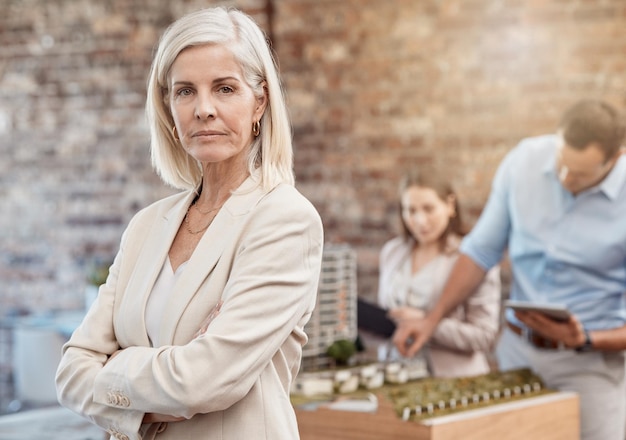 Serious confident and assertive senior project manager leading team in planning Female urban planner standing as her employees design a model in the background Top executive architecture firm