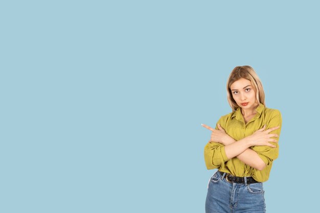 Серьезная уверенная в себе молодая 20-летняя белая блондинка, указывающая в сторону, стоит на синем фоне.