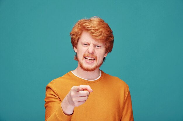 Serious confident young redhead man with beard pointing at you when asking question