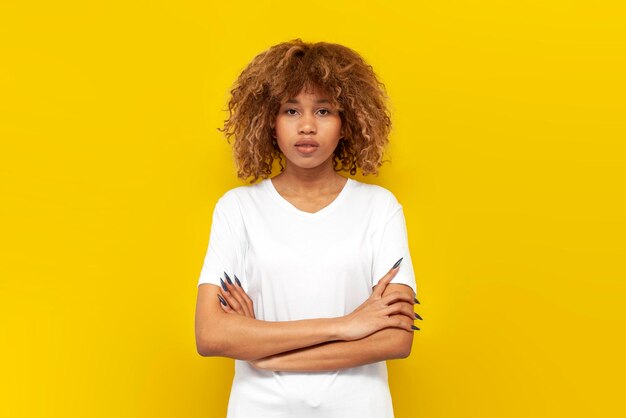 Photo serious curly african american girl in white tshirt stands with her arms crossed