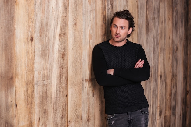 Serious curly young man in black sweater standing with arms crossed