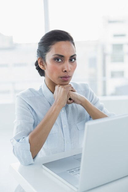 Serious dark haired woman looking at camera sitting at her desk