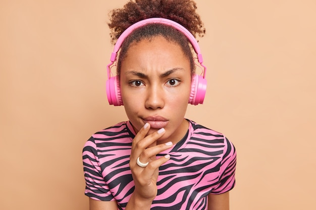 Serious dark skinned Afro American woman looks with attentive gaze at camera raises eyebrows