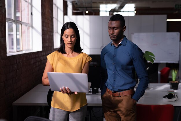 Serious diverse male and female colleague standing in office looking at laptop together. working in business at a modern office.