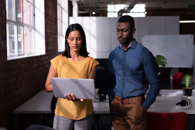 Serious diverse male and female colleague standing in office looking at laptop together. working in business at a modern office.