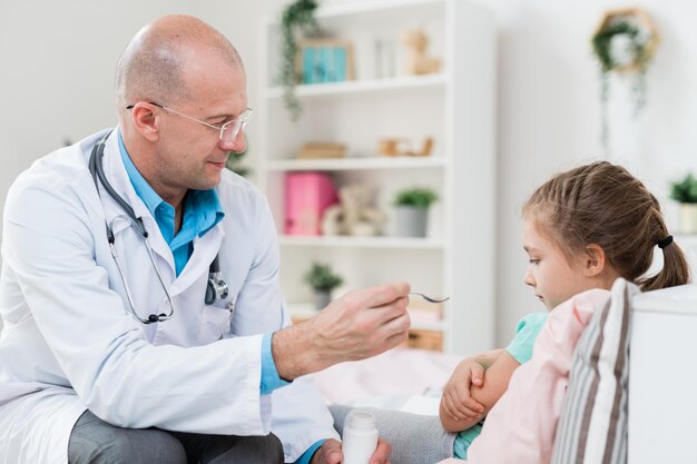 Serious doctor giving medicine to his sick little patient lying in bed