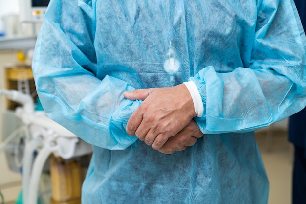 Serious doctor in protective gown is preparing operating patient in modern clinic Male surgeon standing arms crossed at his cabinet