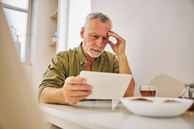 Photo serious elderly gentleman being concerned and looking at his tablet