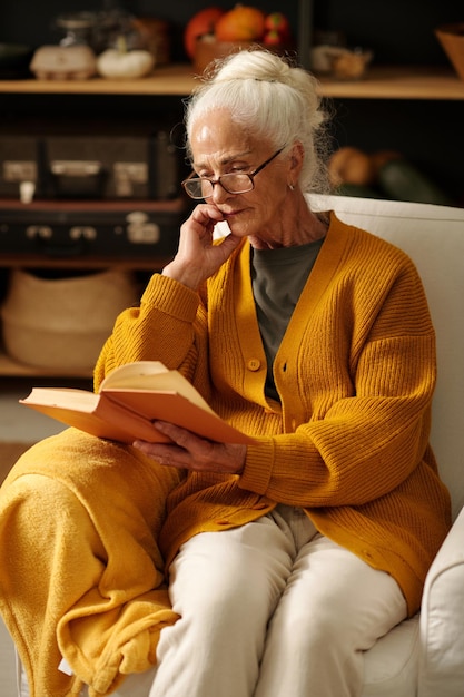 Serious elderly woman with white hair reading interesting book