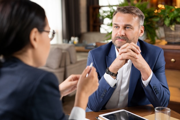 Imprenditore serio in abbigliamento formale che ascolta le spiegazioni di giovani partner o colleghi sui momenti di lavoro