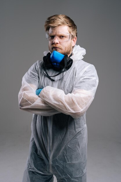 보호복, 안경, 인공호흡기를 착용한 심각한 전염병학자 의료 종사자가 가슴에 손을 얹고 있습니다. 코로나바이러스 COVID-19 전염병의 개념. 스튜디오는 격리된 어두운 배경에서 촬영되었습니다.