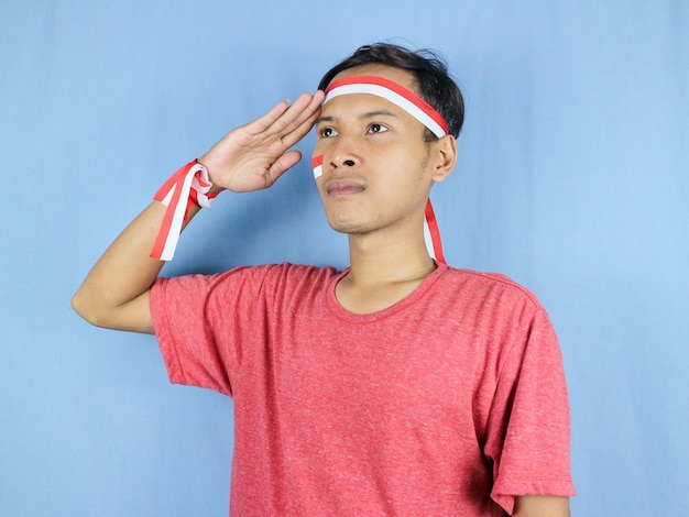 Photo serious expression indonesian man wearing red and white headband posing to salute indonesian flag