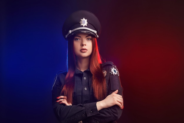 Serious female police officer is posing for the camera against a black background with red and blue ...