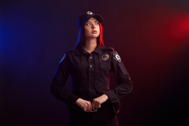 Serious female police officer is posing for the camera against a black background with red and blue ...