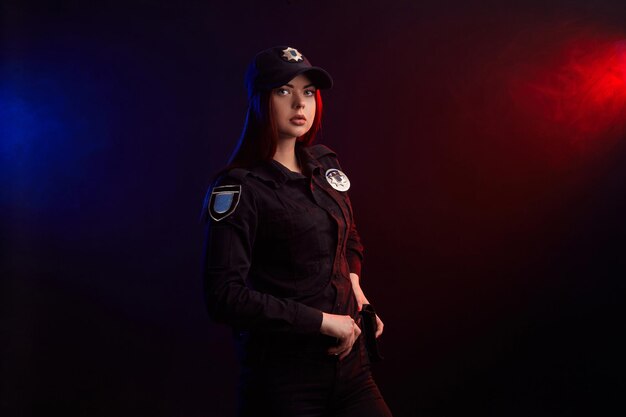 Photo serious female police officer is posing for the camera against a black background with red and blue ...