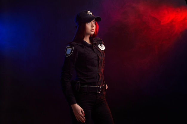 Serious female police officer is posing for the camera against a black background with red and blue ...