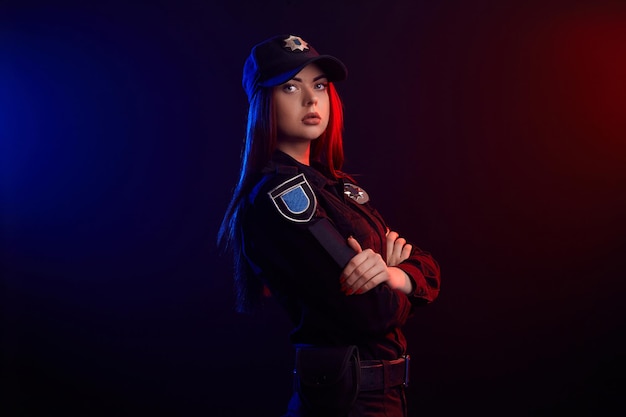 Serious female police officer is posing for the camera against a black background with red and blue ...