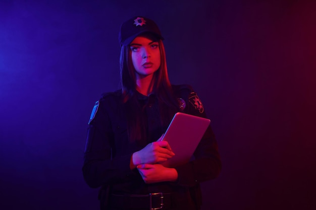 Foto l'ufficiale di polizia femminile serio sta posando per la macchina fotografica su uno sfondo nero con rosso e blu ...