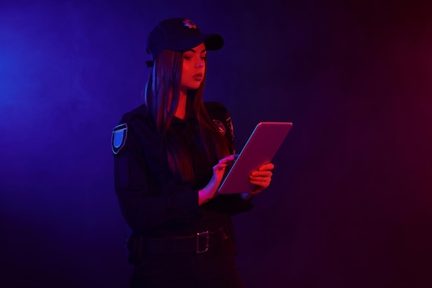 Serious female police officer is posing for the camera against a black background with red and blue ...