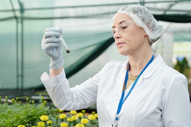 Serious female researcher looking at flask with soil sample