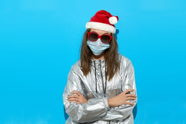 Serious female wearing Santa hat and protective mask and red sunglasses