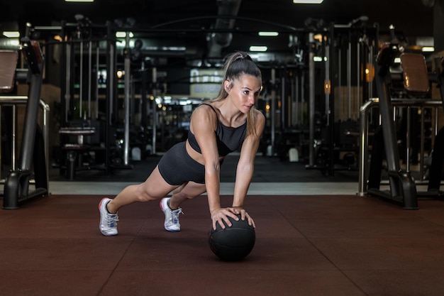 Serious fit sportswoman doing medicine ball plank exercise in gym