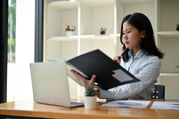 A serious and focused Asian businesswoman examining business documents at her desk