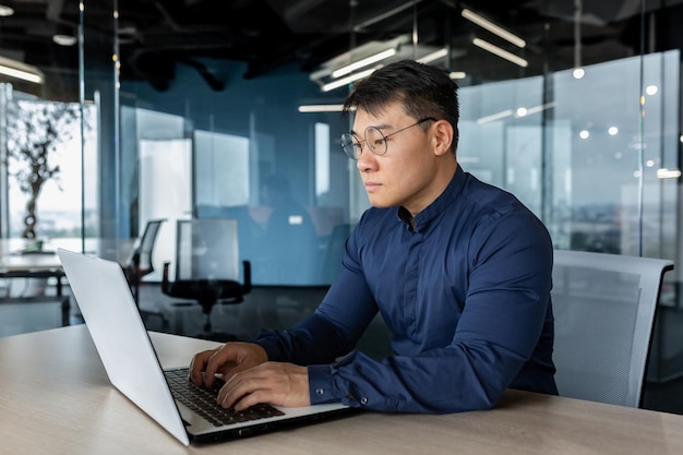 Serious and focused businessman working with laptop man in glasses and shirt inside office building