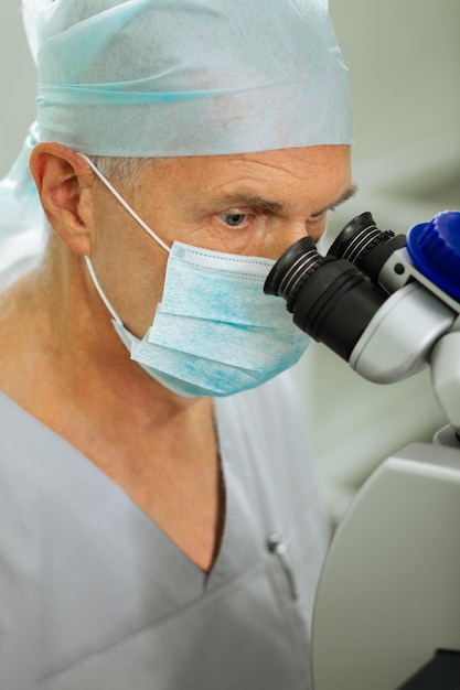 Serious focused man looking into the microscope lenses