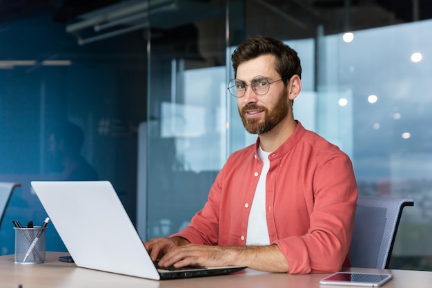 Serious and focused mature businessman in red shirt wearing glasses looking at camera young man at