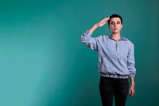 Serious focused woman doing patriotic greeting with honor and respect for veterans servicemen. Caucasian female doing military soldier salute while looking at camera standing over isolated background.