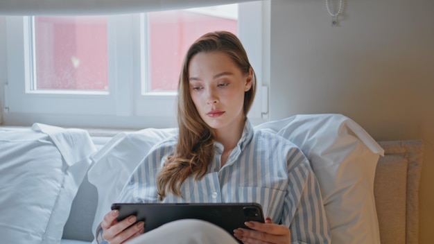Serious freelancer working bed looking tablet screen closeup Calm businesswoman