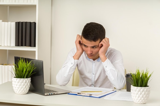 Serious frustrated asian businessman suffering from headache migraine at workplace feeling tired exhausted chronic work stress