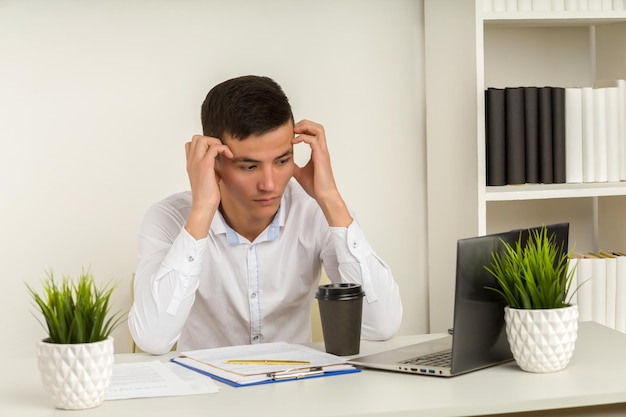 Serious frustrated asian businessman suffering from headache migraine at workplace feeling tired exhausted chronic work stress