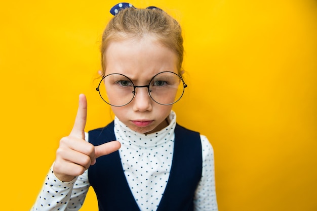 Serious funny child girl with index finger on yellow