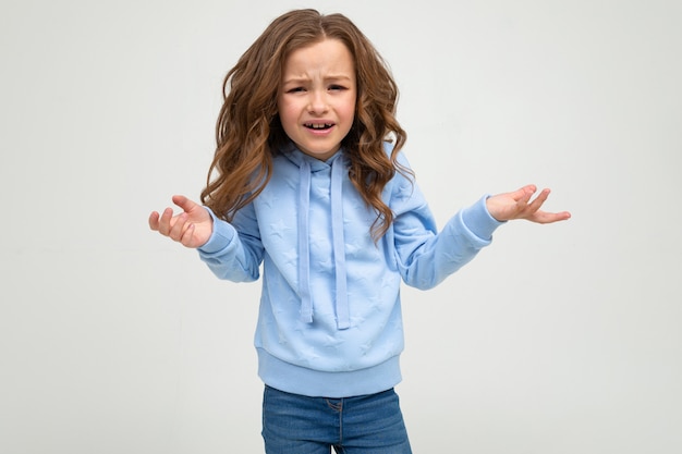 Serious girl in casual blue hoodie indignant on a white wall with blank space