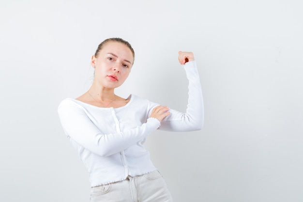 La ragazza seria sta mostrando il suo muscolo su priorità bassa bianca