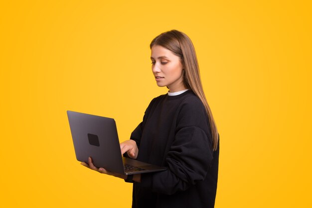 진지하고 화려한 젊은 여성이 서 있는 동안 노트북을 사용하고 있습니다.